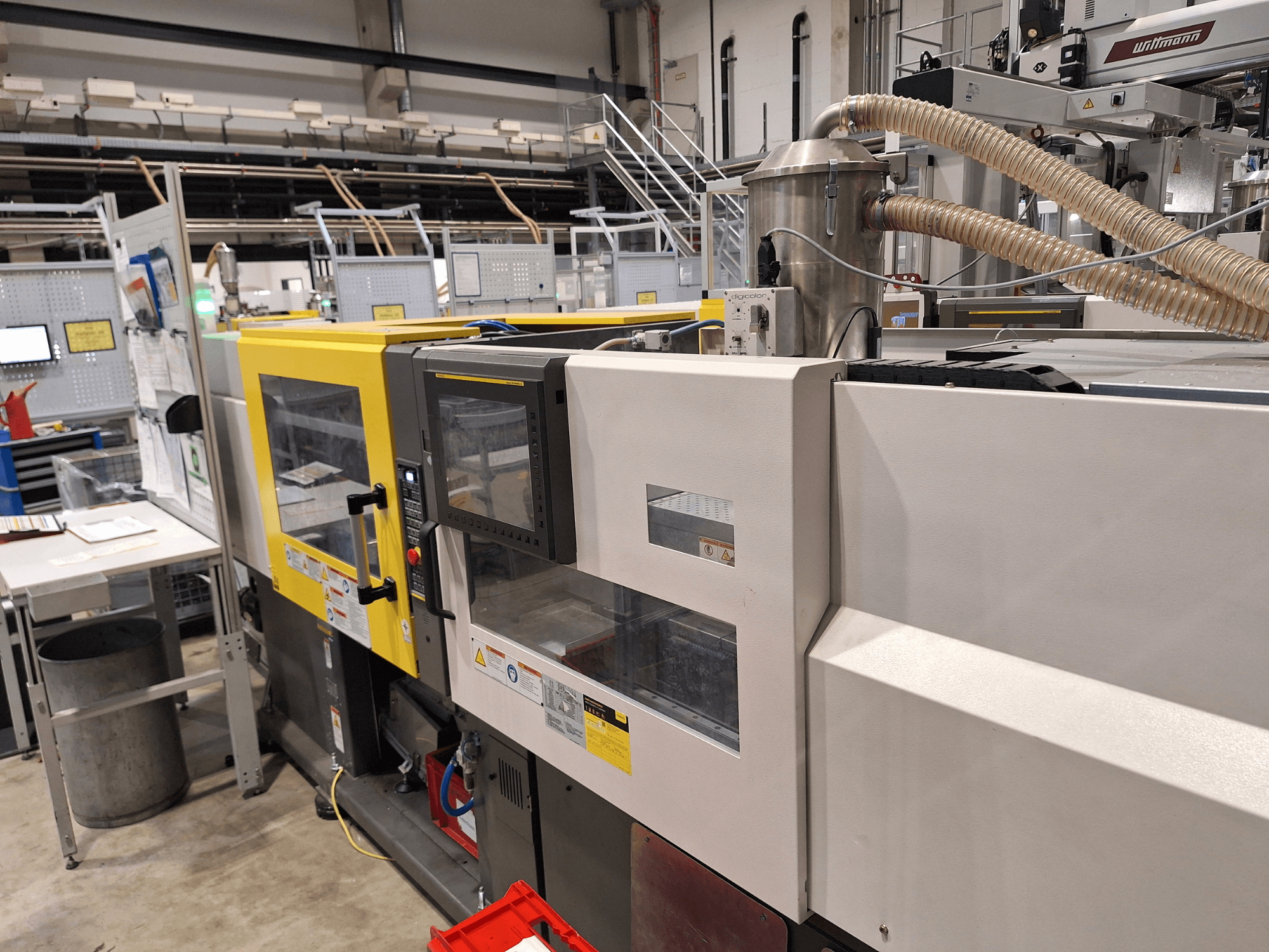 Вид спереду різнокольорової машини для лиття під тиском, з жовтою та сірою секціями, з панеллю керування та вихлопною системою.