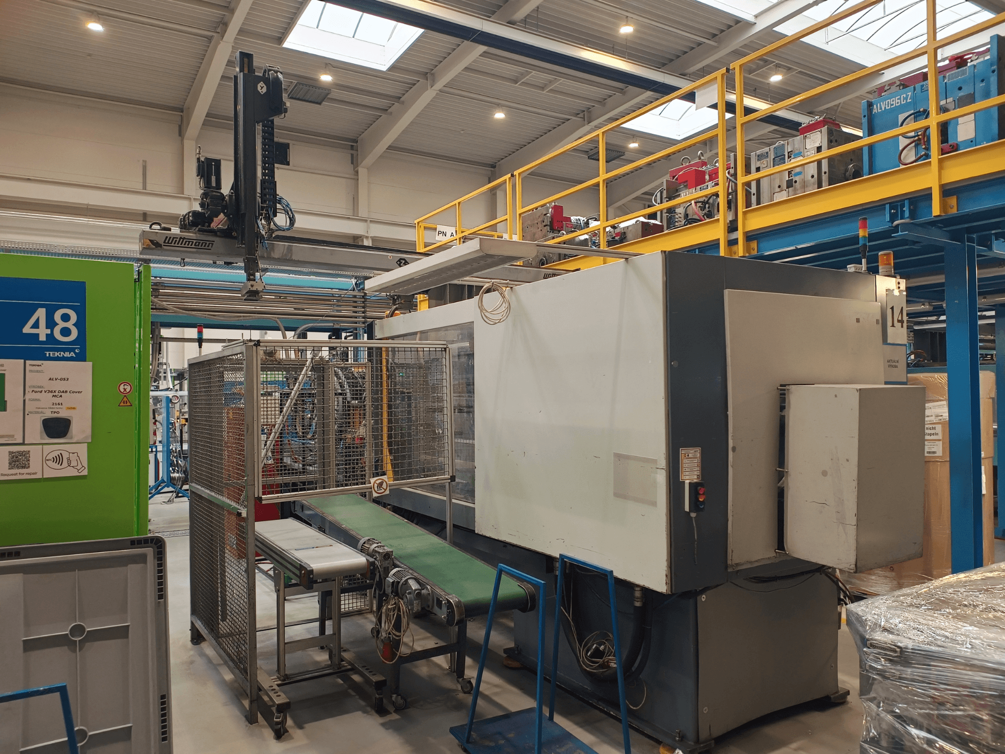 Обладнання для промислової автоматизації з зеленим конвеєром, позначеним "48", і мостовим краном; вигляд збоку машини на заводському майданчику.